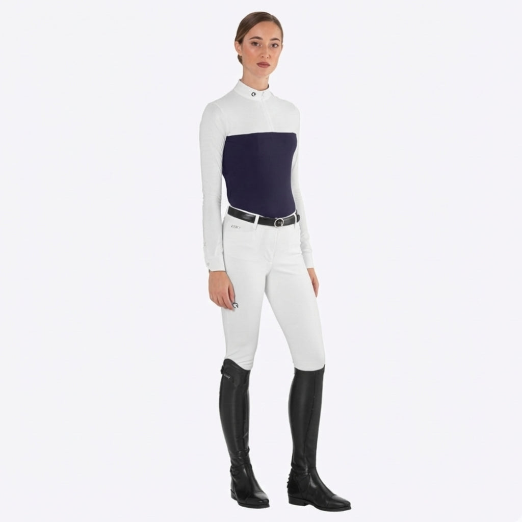 Woman wearing navy and white long sleeve riding shirt, white breeches, black belt, and tall black riding boots